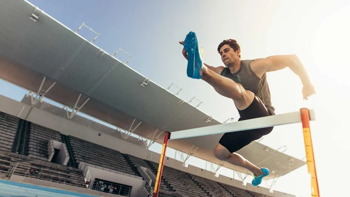 Olympics picture of a man completing a race and jumping over an obstacle.